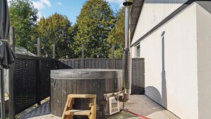 Un jardin avec un jacuzzi, une chaise en bois et un tuyau d’arrosage.
