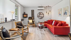 Un salon moderne avec un canapé rouge, des fauteuils en cuir, une table basse en verre et une cheminée.