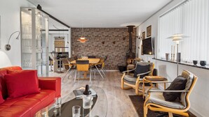 Un salon moderne avec un canapé rouge, une table basse en verre et un coin repas agrémenté d’un mur en briques.