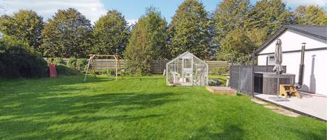 A well-maintained backyard with a wooden swing set, a greenhouse, and a barbecue area.