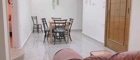 Un comedor con una mesa y sillas de madera, piso de baldosas y plantas colgantes en las paredes.