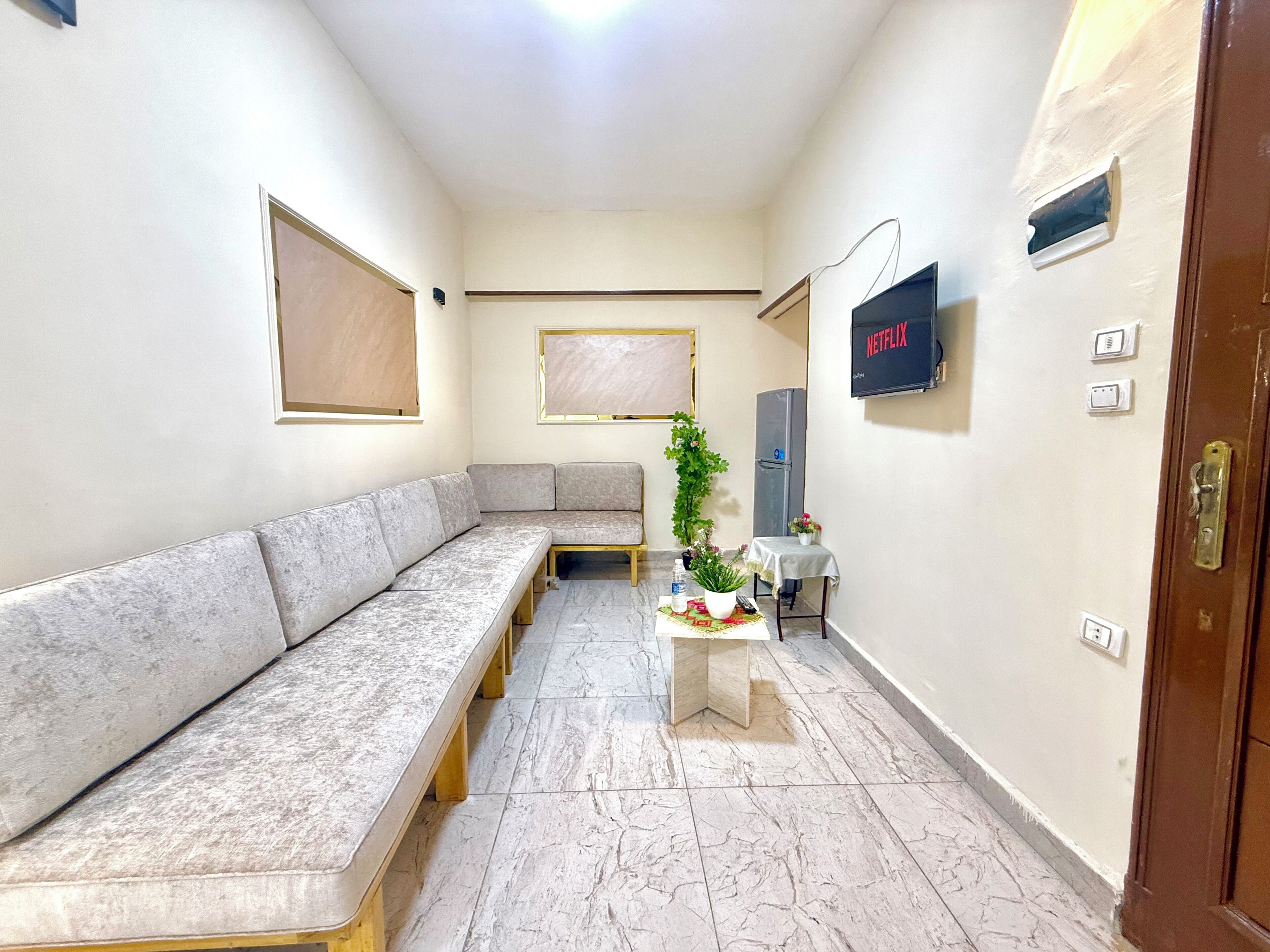 Una sala de estar moderna con un sofá seccional, una mesita con una planta, un televisor y un refrigerador.