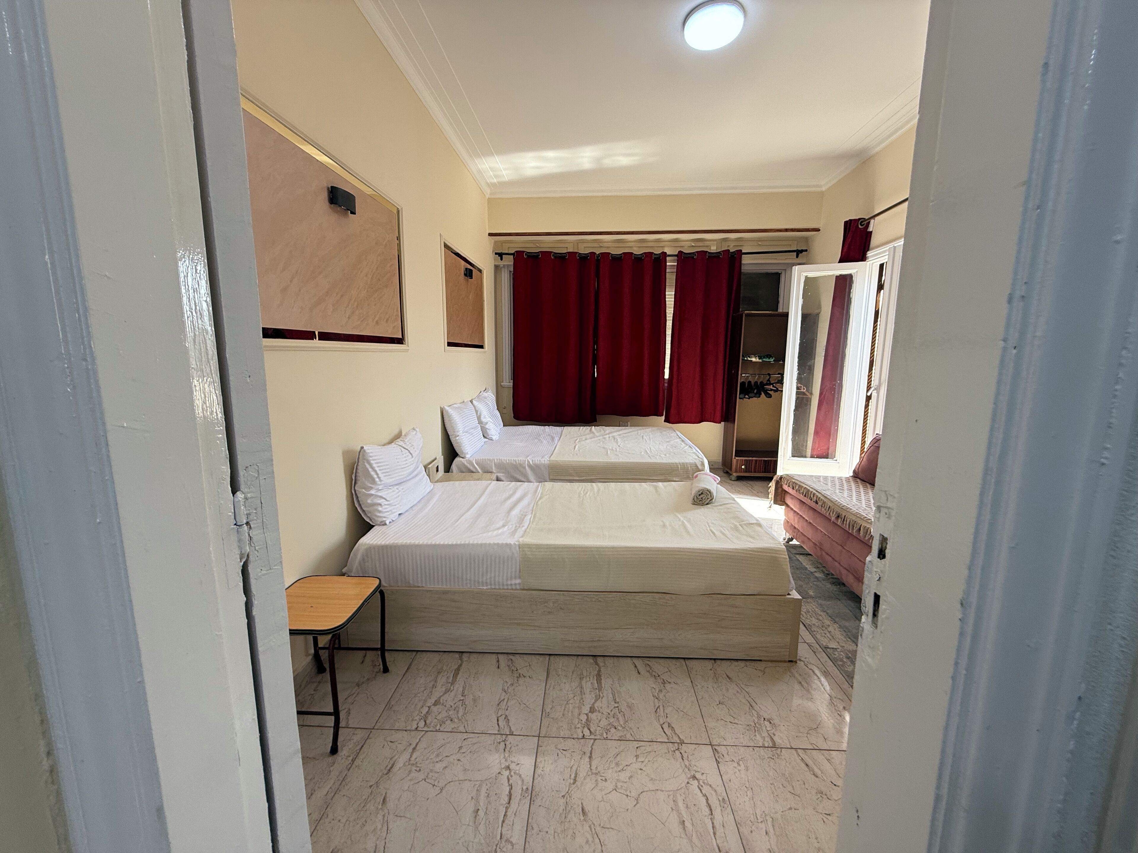 A bedroom with two beds, a wooden table, a wardrobe, and a mirror.
