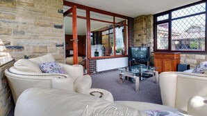 A living room with a stone wall, a glass coffee table, and a television. - Stunning Residence set on Cliffside in Scarborough (Scarborough)