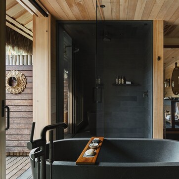 A modern bathroom with a freestanding bathtub, a glass shower enclosure, and wooden paneling.
