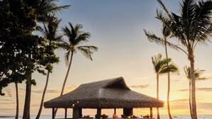 A beach bar with thatched roof, surrounded by palm trees and wooden chairs. - Kona Village, A Rosewood Resort (Kailua-Kona)