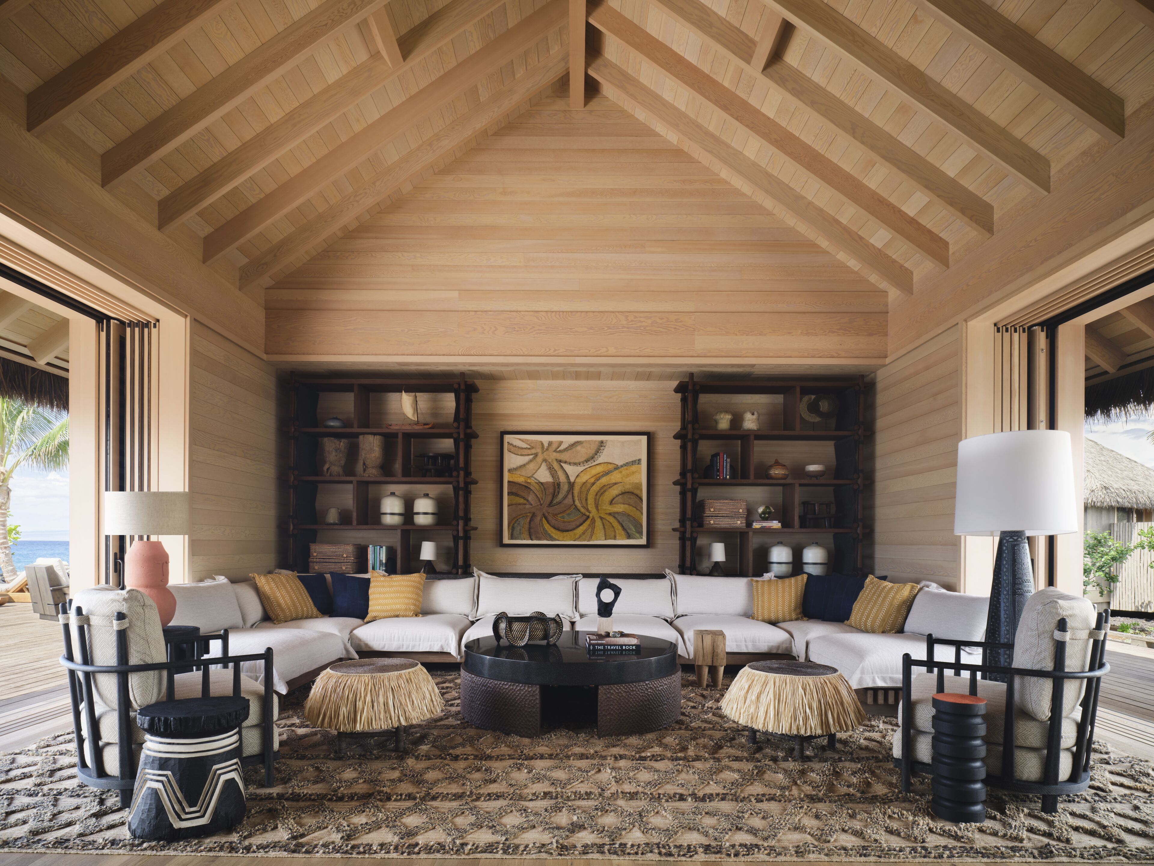 Un vaste espace de vie doté d’un haut plafond, de bibliothèques encastrées en bois, d’un grand tableau abstrait et d’un coin salon confortable avec une table basse.