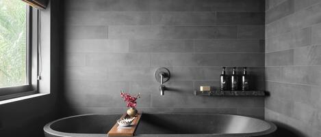 A modern bathroom with a freestanding bathtub, a wooden tray, and a small shelf with toiletries.