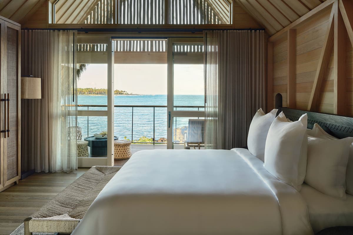 A bedroom with a large bed, a view of the sea, and a balcony with a chair and table.