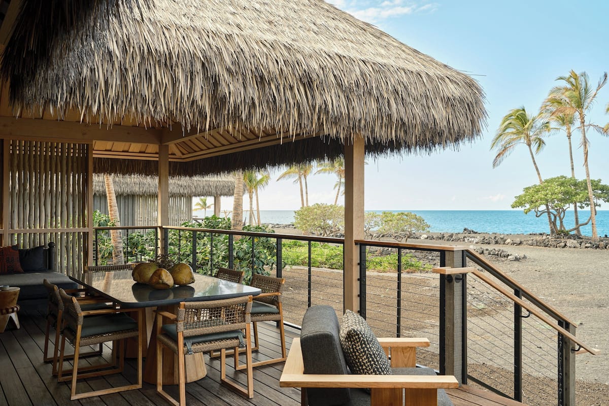 A wooden deck with a thatched roof, outdoor furniture, and a view of the ocean.