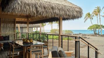A wooden deck with a thatched roof, outdoor furniture, and a view of the ocean.