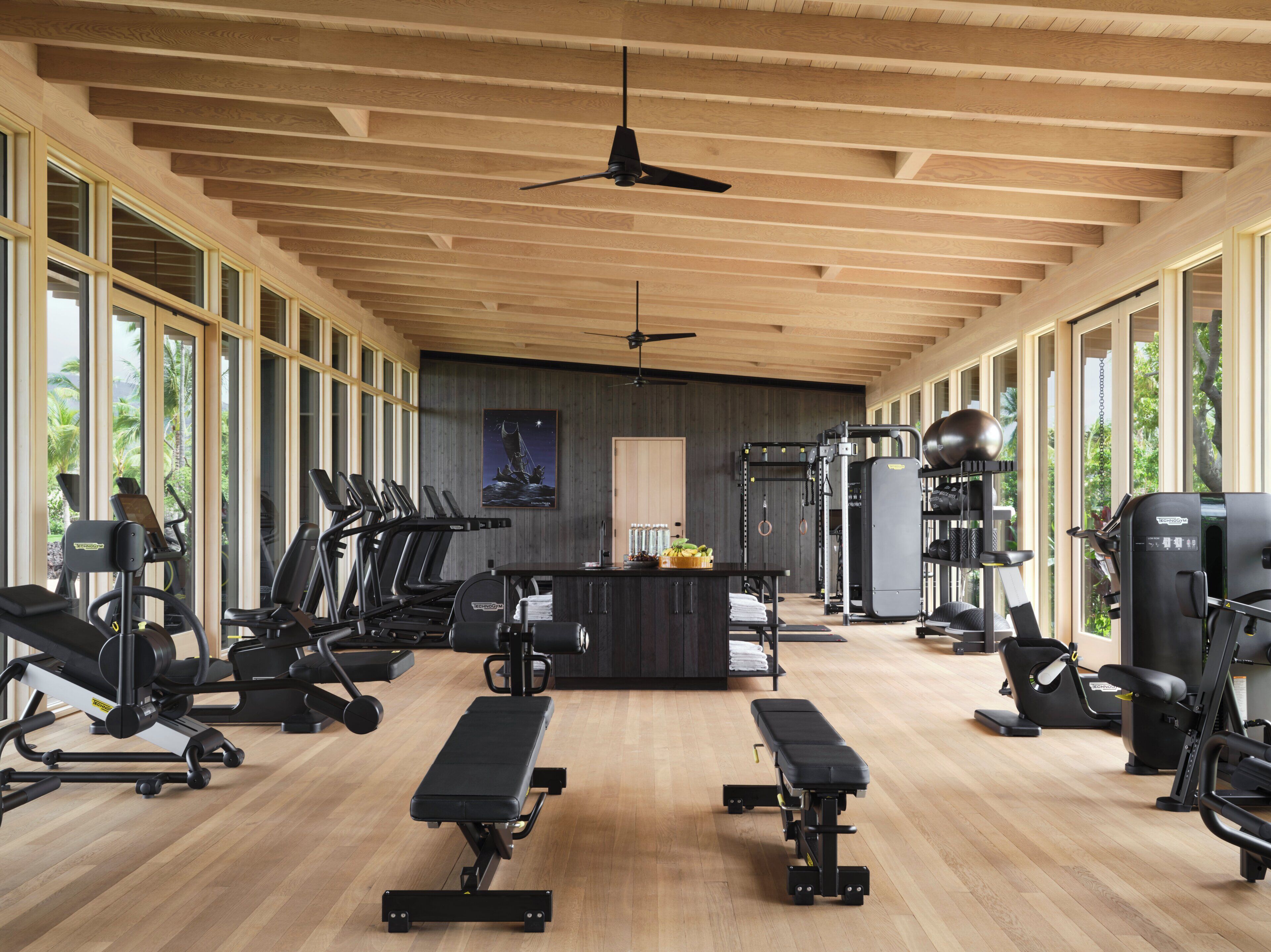 A spacious gym with various exercise equipment, large windows, and a wooden ceiling.
