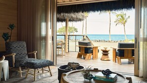 A room with a view of the beach, featuring a wooden deck, a chair, a table with books, and a plant. - Kona Village, A Rosewood Resort (Kailua-Kona)