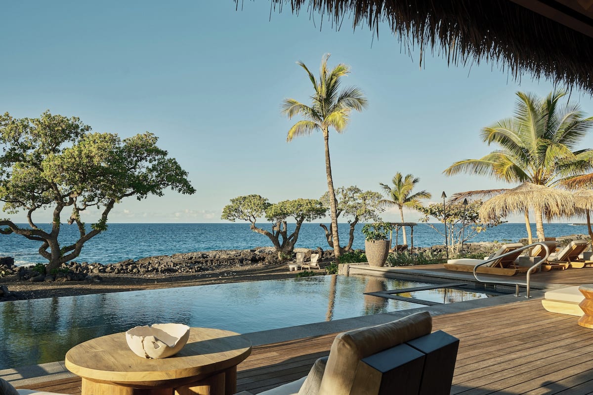A poolside area with lounge chairs, a wooden deck, and a view of the ocean.