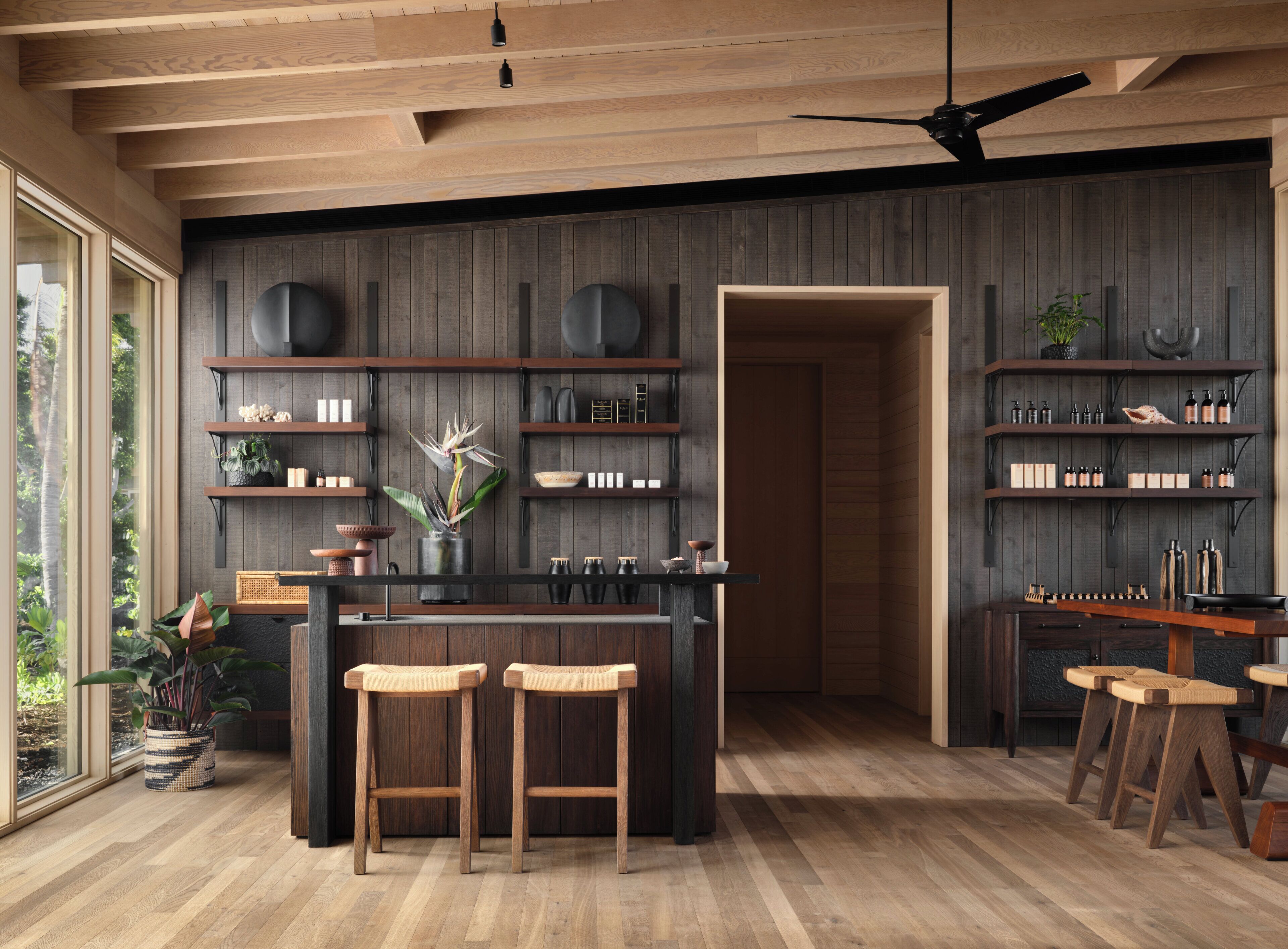 A modern kitchen with wooden shelves, a central island with stools, and a ceiling fan.