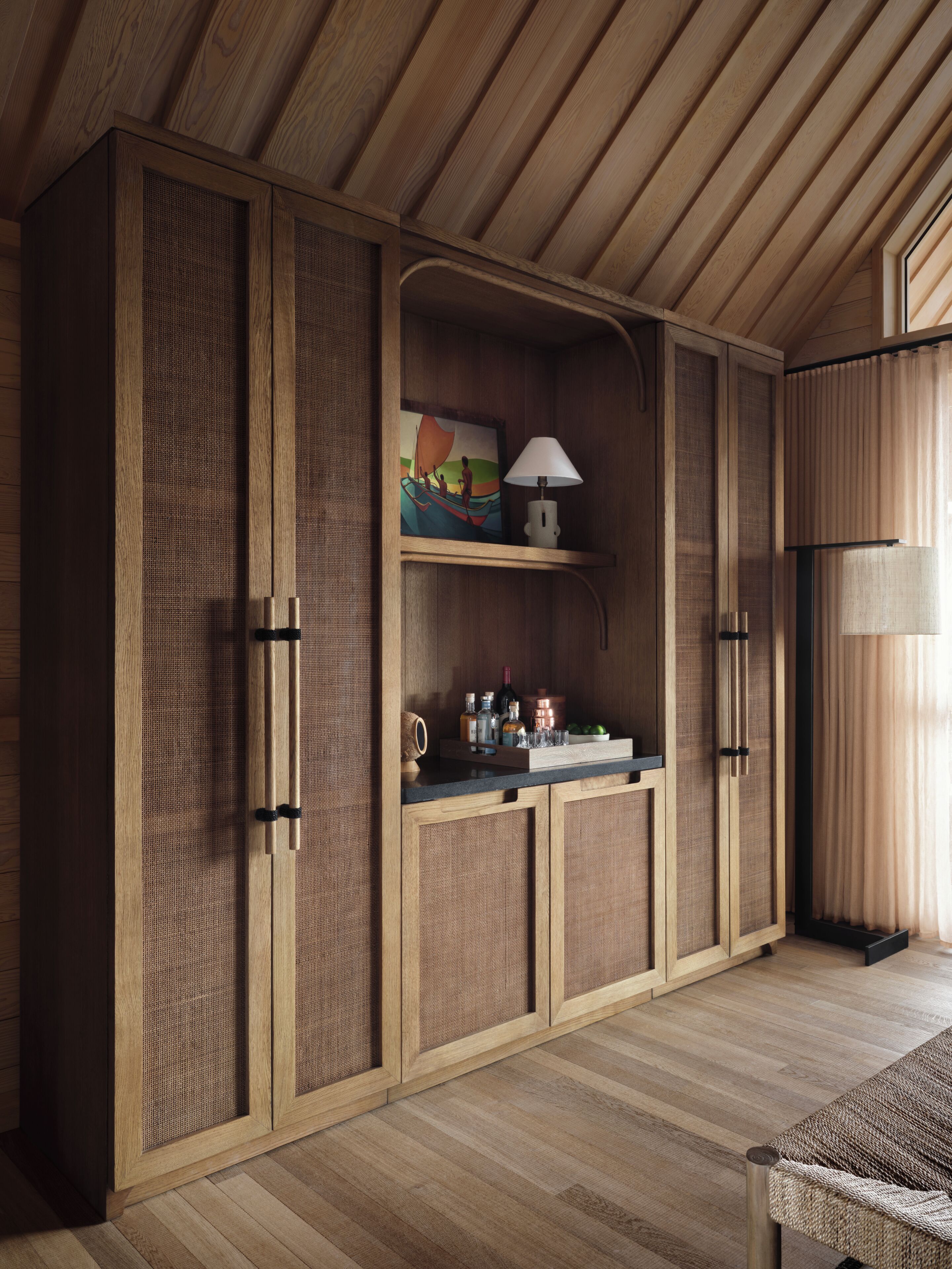 Un mueble de madera con paneles de diseño tejido, una repisa con adornos y una lámpara.