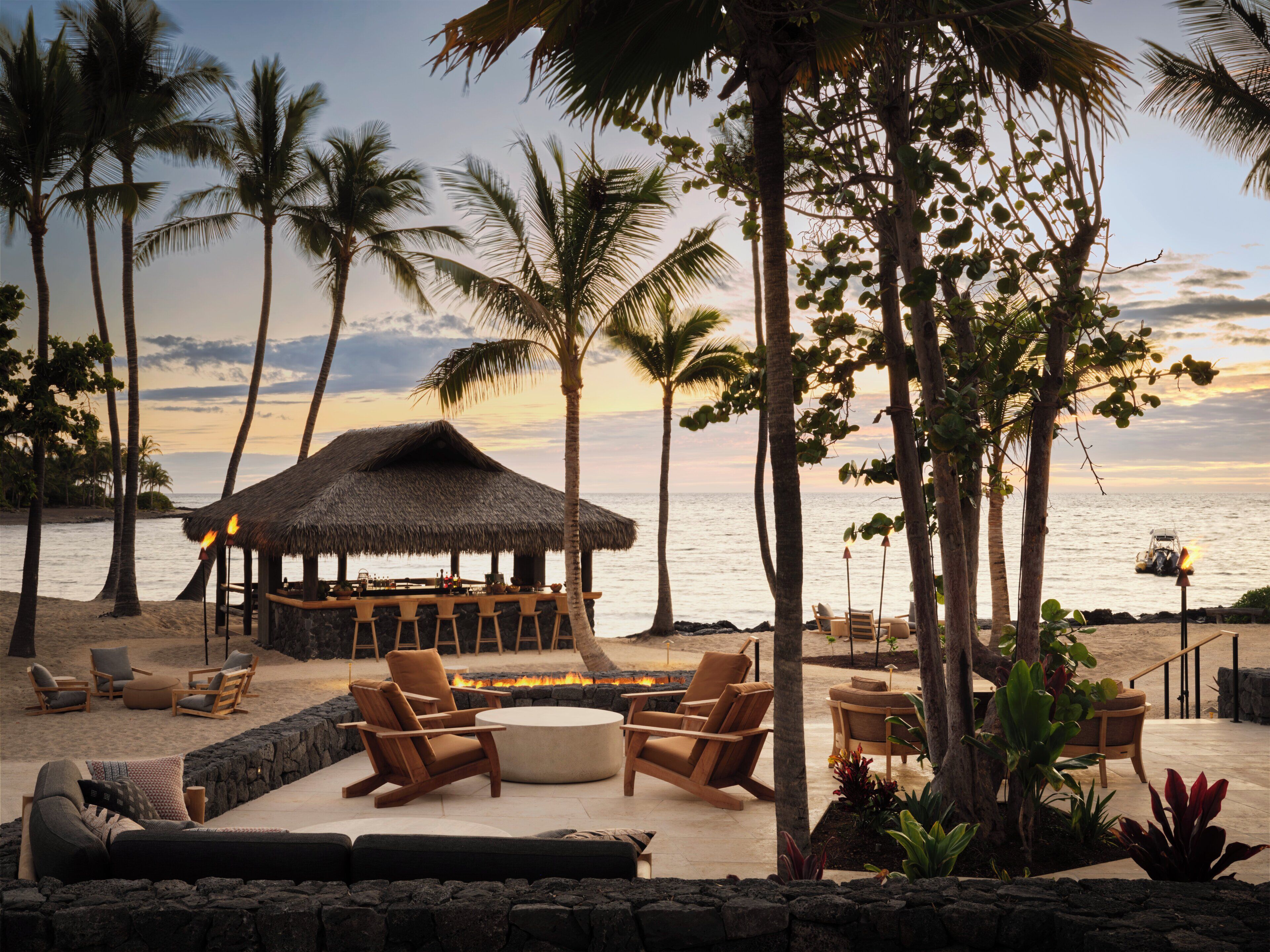 A beachside lounge with a thatched-roof bar, outdoor seating, and a fire pit.