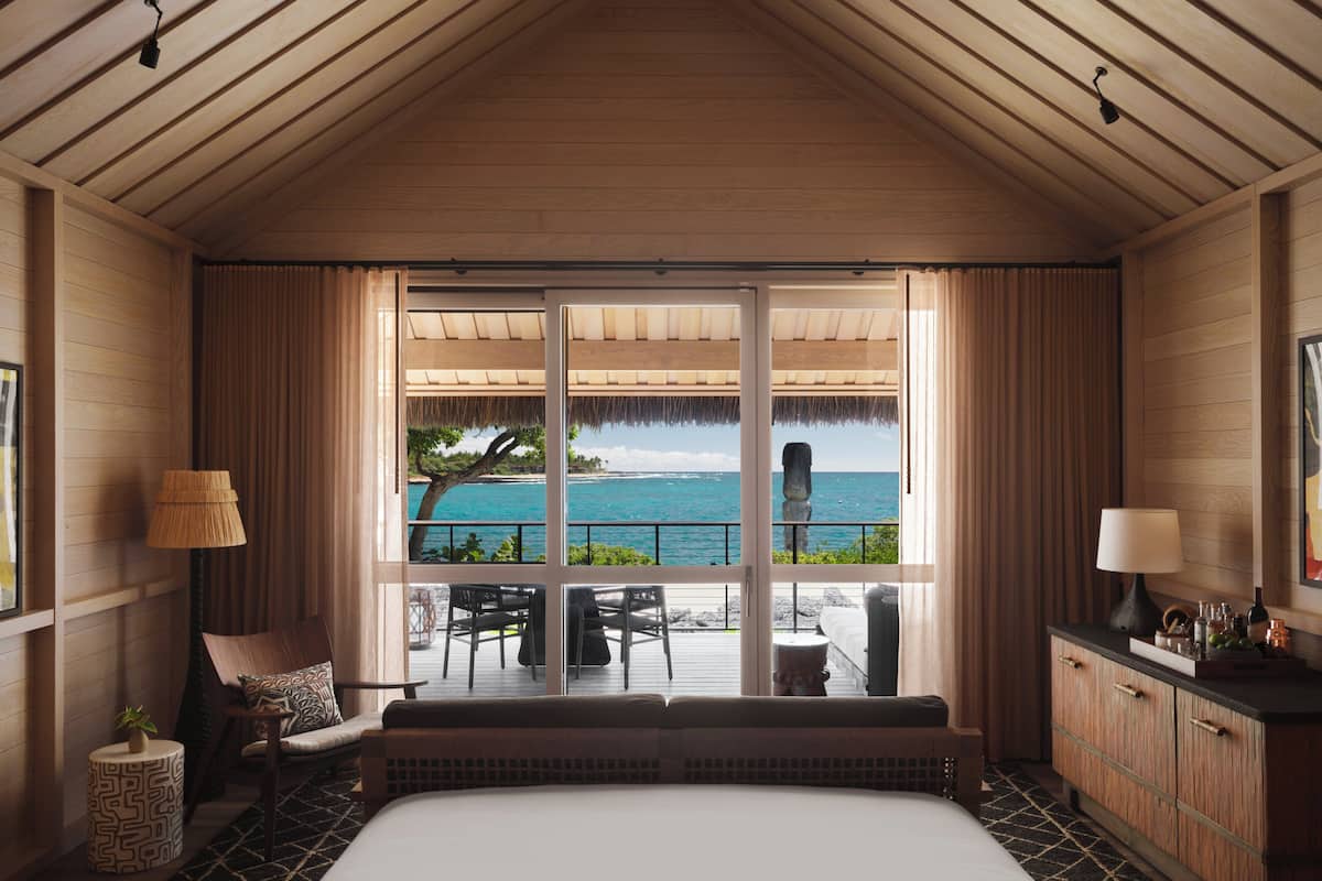 A room with a large bed, a seating area with a view of the ocean, and a wooden ceiling.