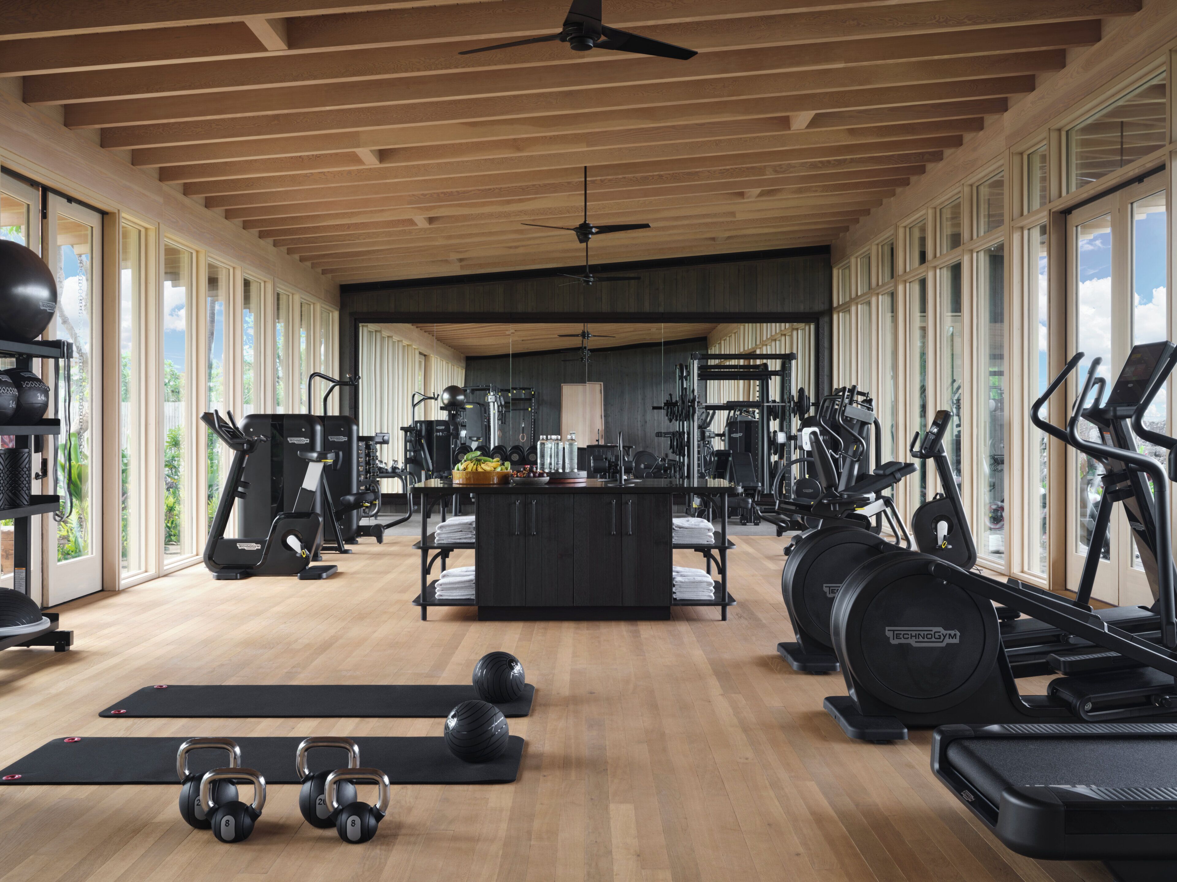 A spacious gym with various exercise equipment, large windows, and a wooden ceiling.