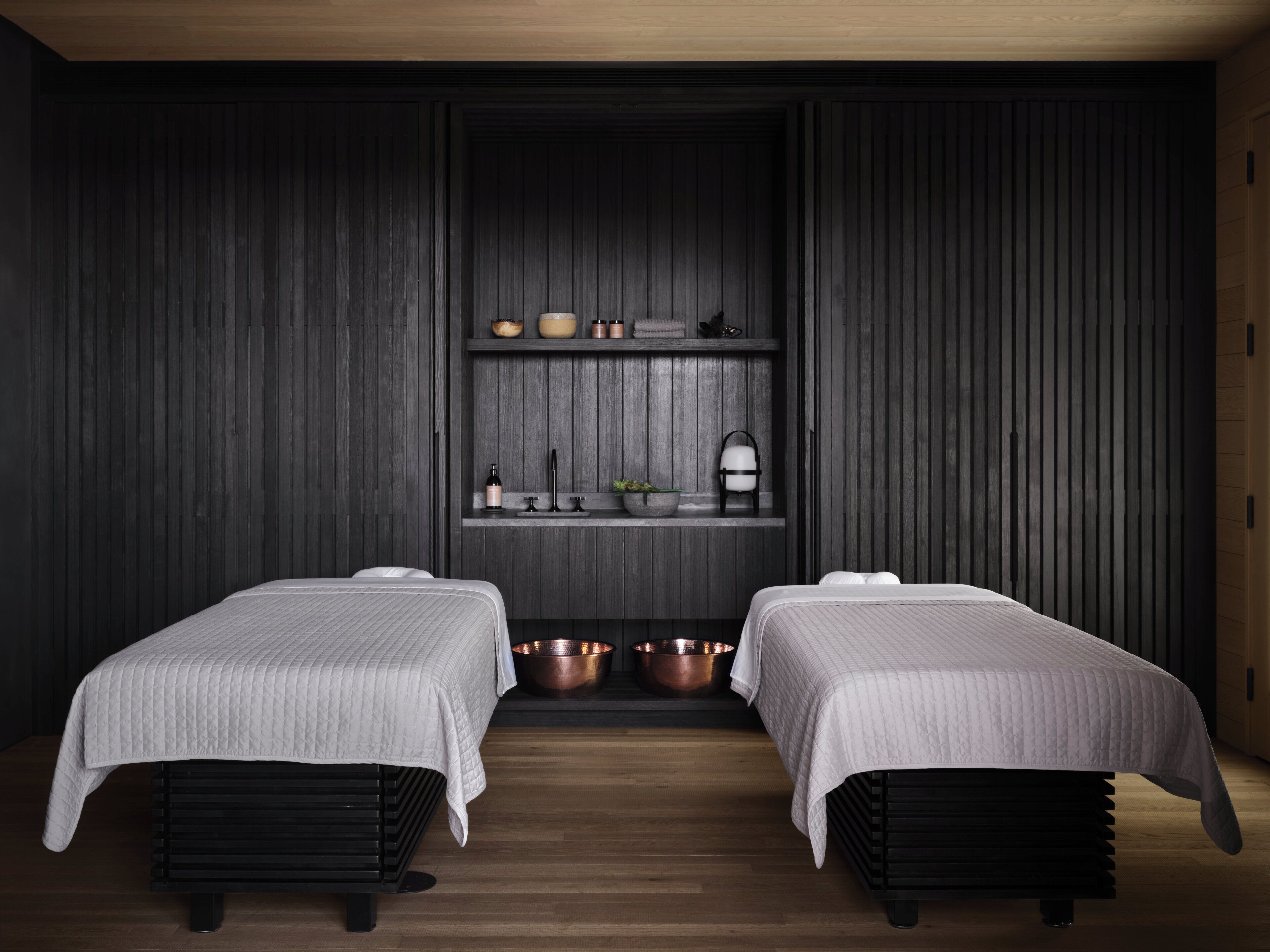 A modern room with two beds, dark wooden walls, a shelf with decorative items, and a wooden floor.
