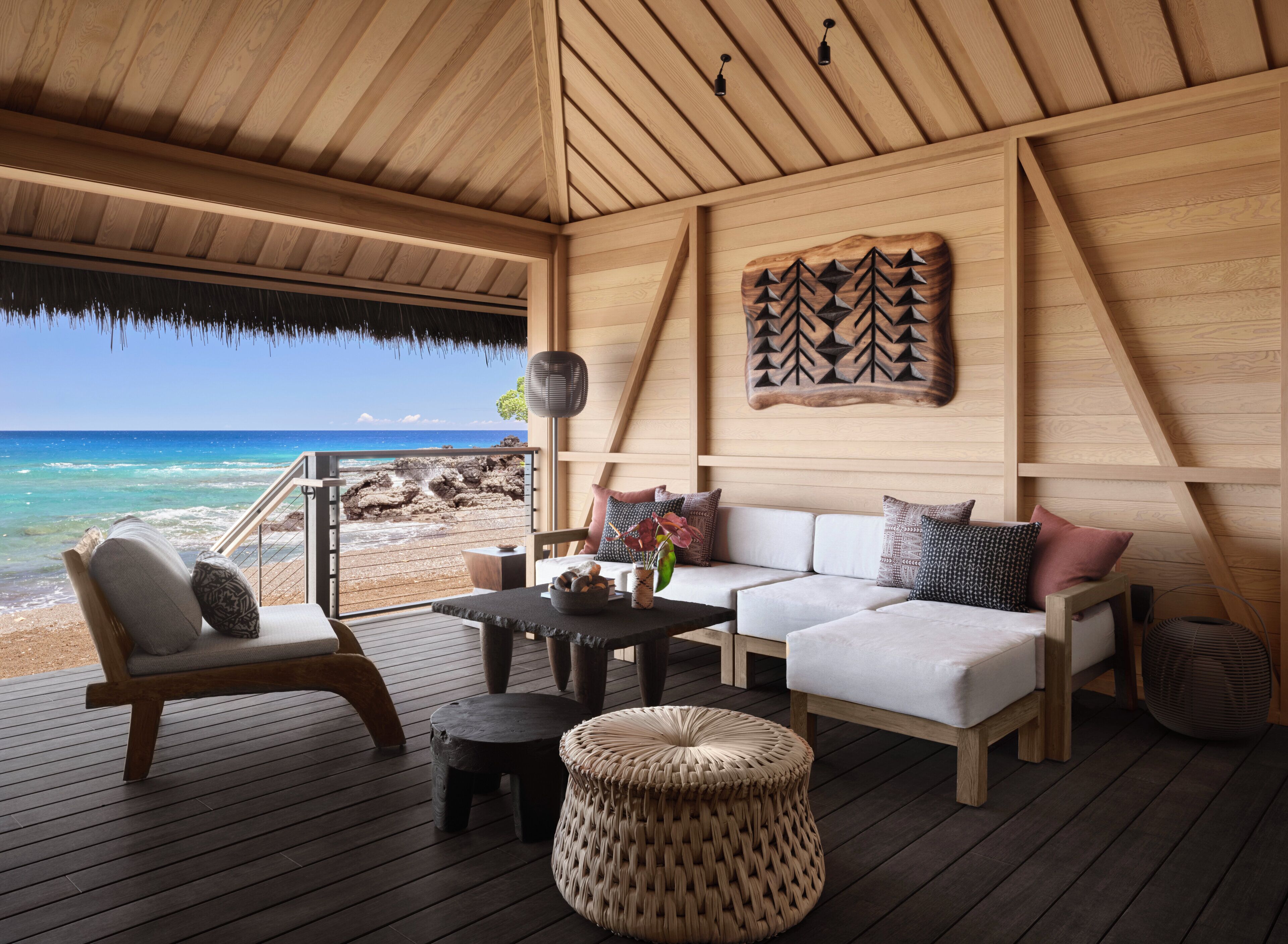 A wooden deck with a sofa, chairs, and a table, overlooking a beach.