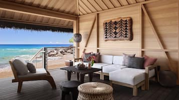 A wooden deck with a sofa, chairs, and a table, overlooking a beach.