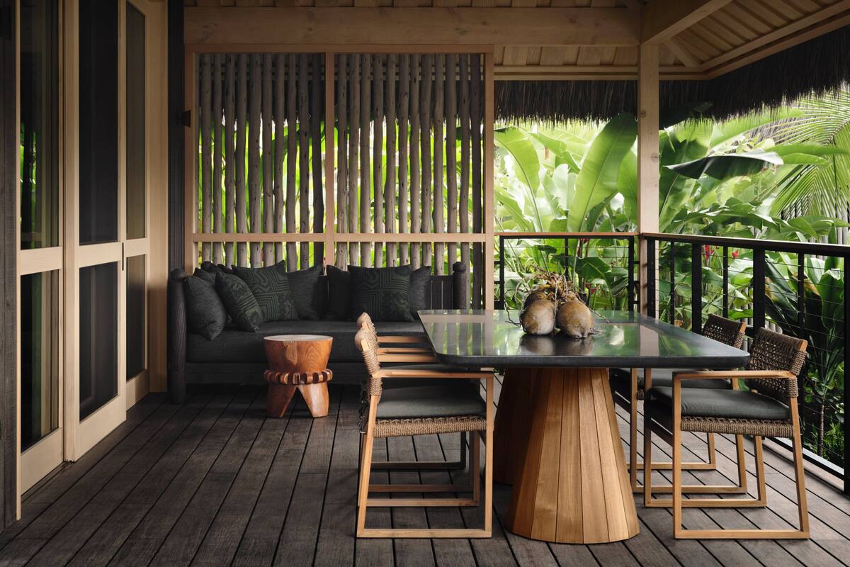 A wooden deck with a table and chairs, a sofa, and a decorative wooden stool.