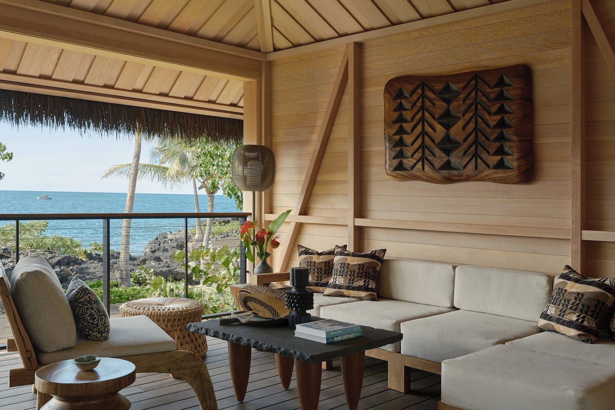 A cozy lounge area with a wooden ceiling, a sofa set, a coffee table, and a view of the ocean.