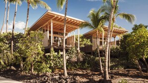 A modern house with a wooden deck, surrounded by palm trees and lush vegetation. - Kona Village, A Rosewood Resort (Kailua-Kona)