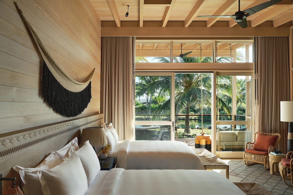 A bedroom with two beds, a hammock, and a view of a tropical garden.
