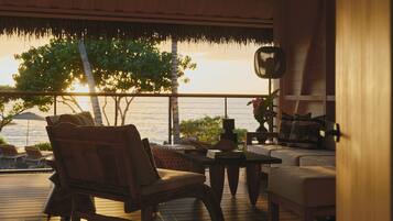 A wooden deck with a view of the ocean, a chair, a table, and a sofa.