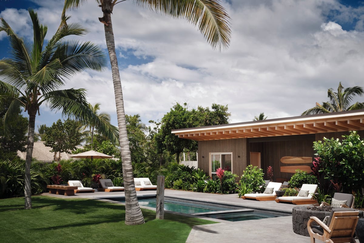 A modern poolside area with lounge chairs, a pool, and a building with a wooden pergola.