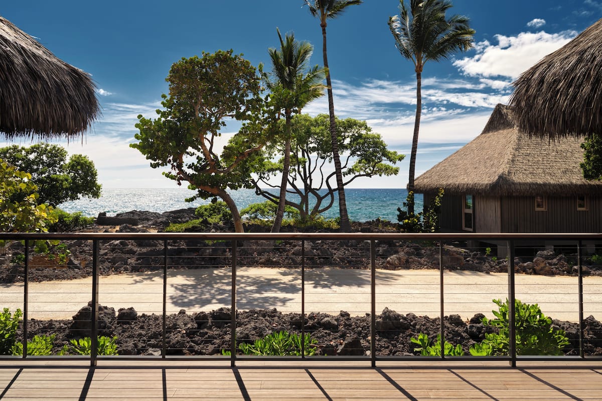 A beach view with thatched-roof huts, palm trees, and a wooden deck.