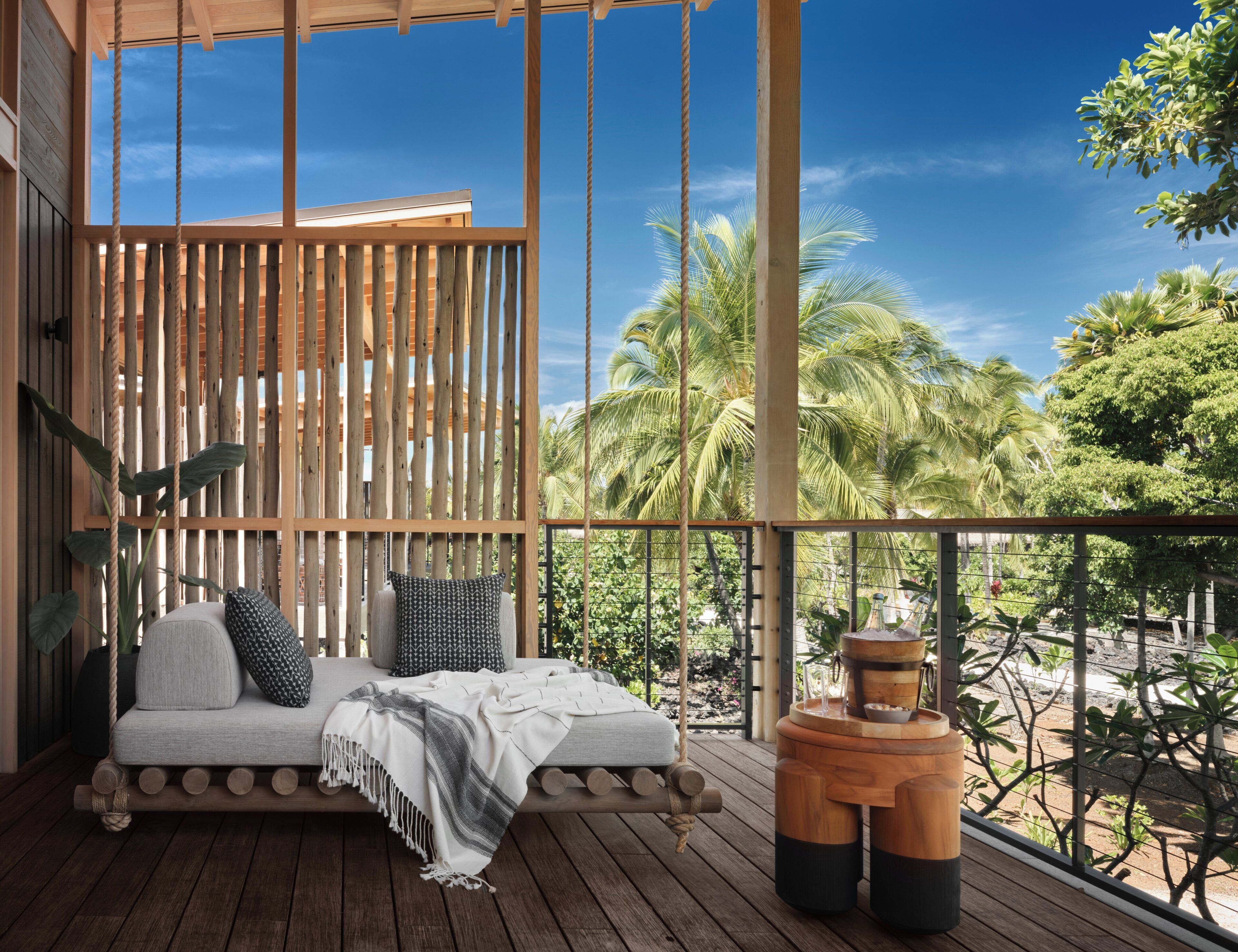 Un terrazza in legno con un'area salotto imbottita, un piccolo tavolino e vista su palme.