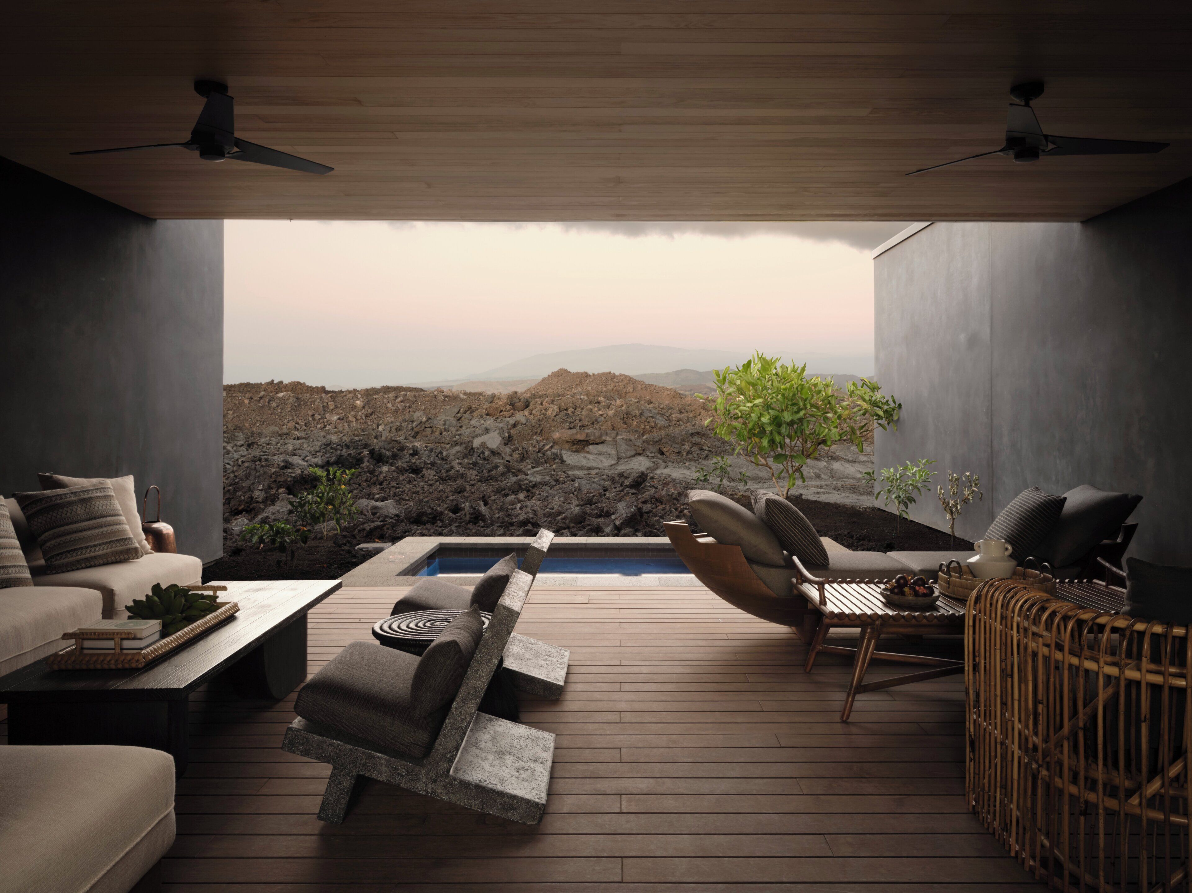 A modern outdoor lounge area with a pool, seating, and a view of rocky terrain.