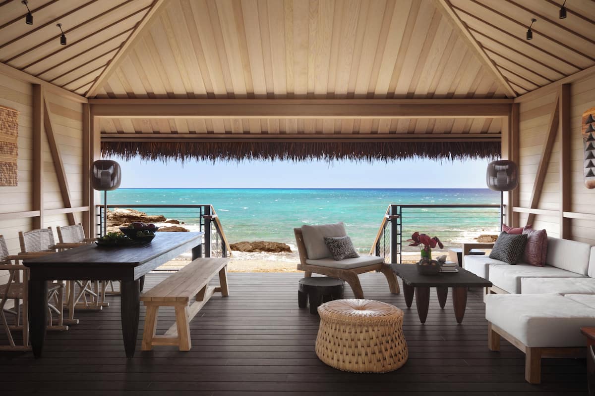 An open-air deck with wooden furniture, a thatched roof, and a view of the ocean.