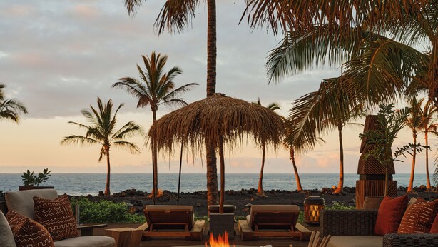 An outdoor seating area with a fire pit, lounge chairs, and a view of the ocean. - Kona Village, A Rosewood Resort (Kailua-Kona)