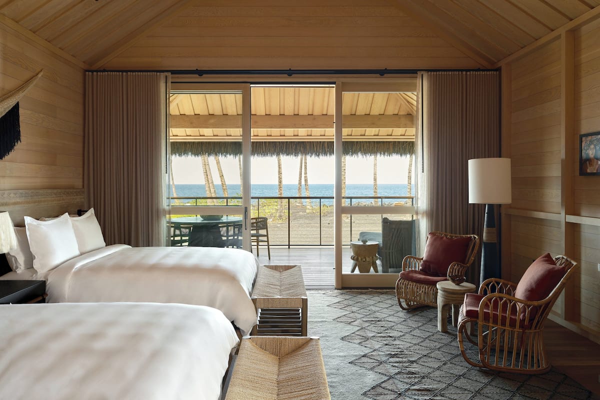 A hotel room with two beds, a balcony with a view of the beach, and a wicker chair.