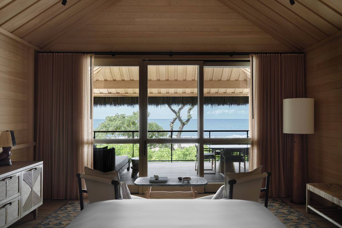 A hotel room with a large bed, a desk, a chair, a table, and a view of the ocean.
