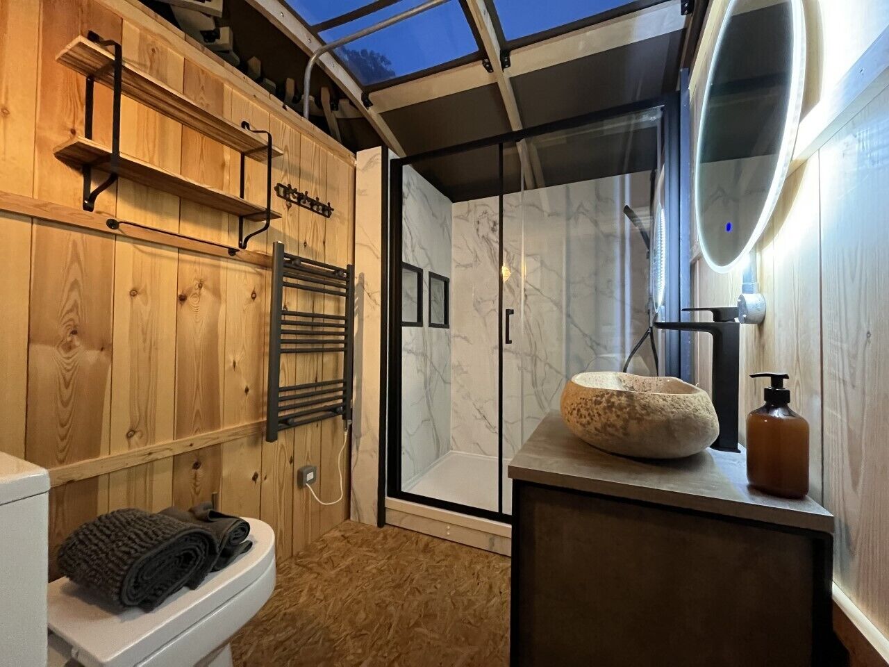 A wooden interior with a glass shower enclosure, a white toilet, and a sink with a marble basin.