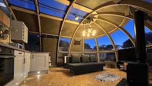 A cozy interior with a curved ceiling, a sofa, a fireplace, and a kitchen area. - Sunrise Dome Tent (Tenby)
