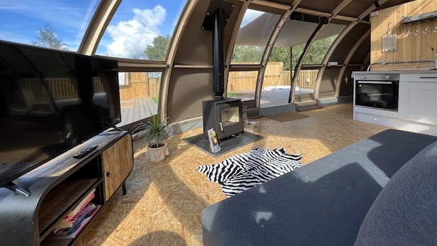 A cozy, semi-open living space with a television, a fireplace, and a kitchen area. - Sunrise Dome Tent (Tenby)