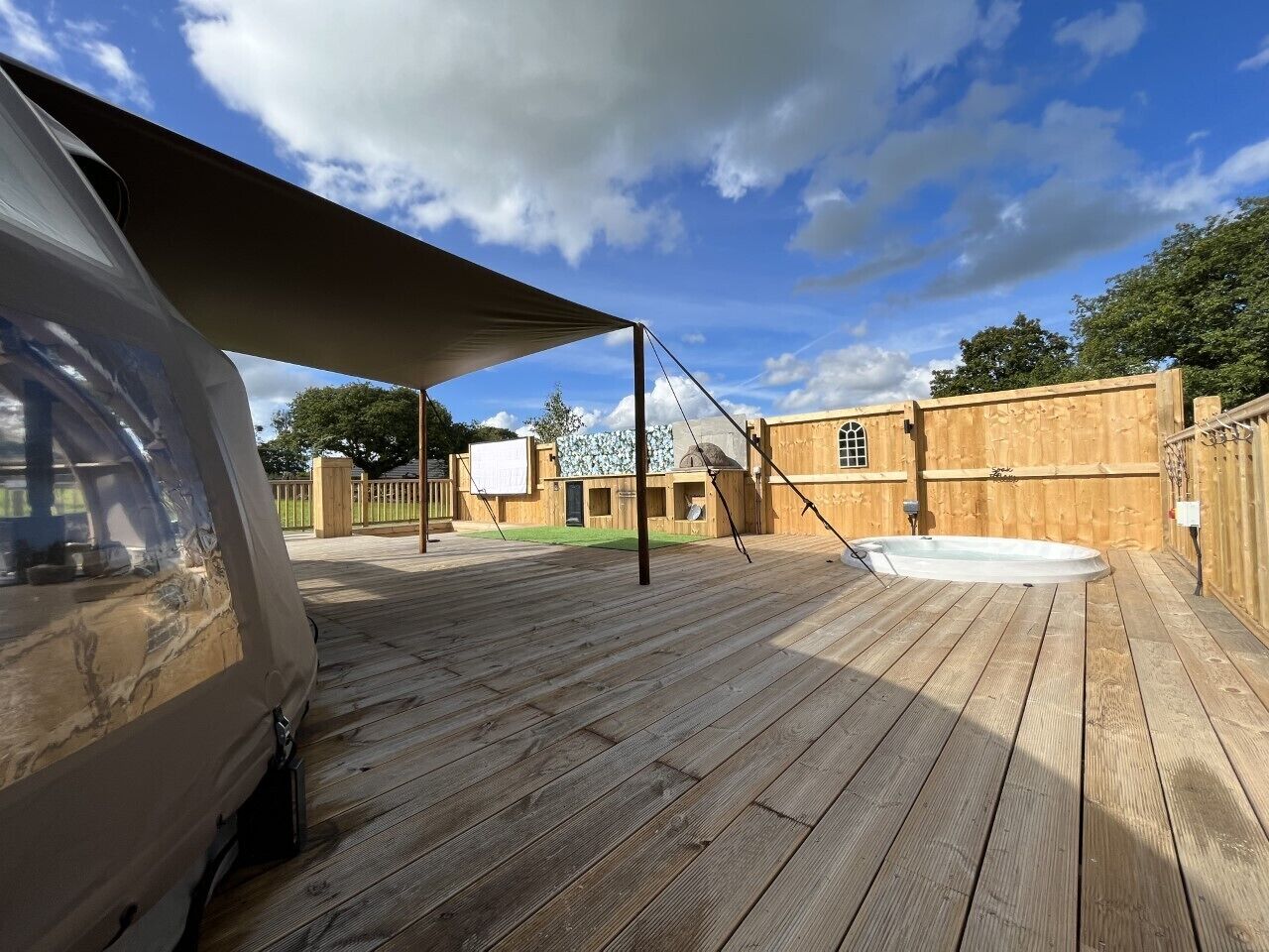 A wooden deck with a hot tub, a covered area, and a building in the background.
