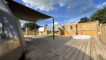 A wooden deck with a hot tub, a covered area, and a building in the background.