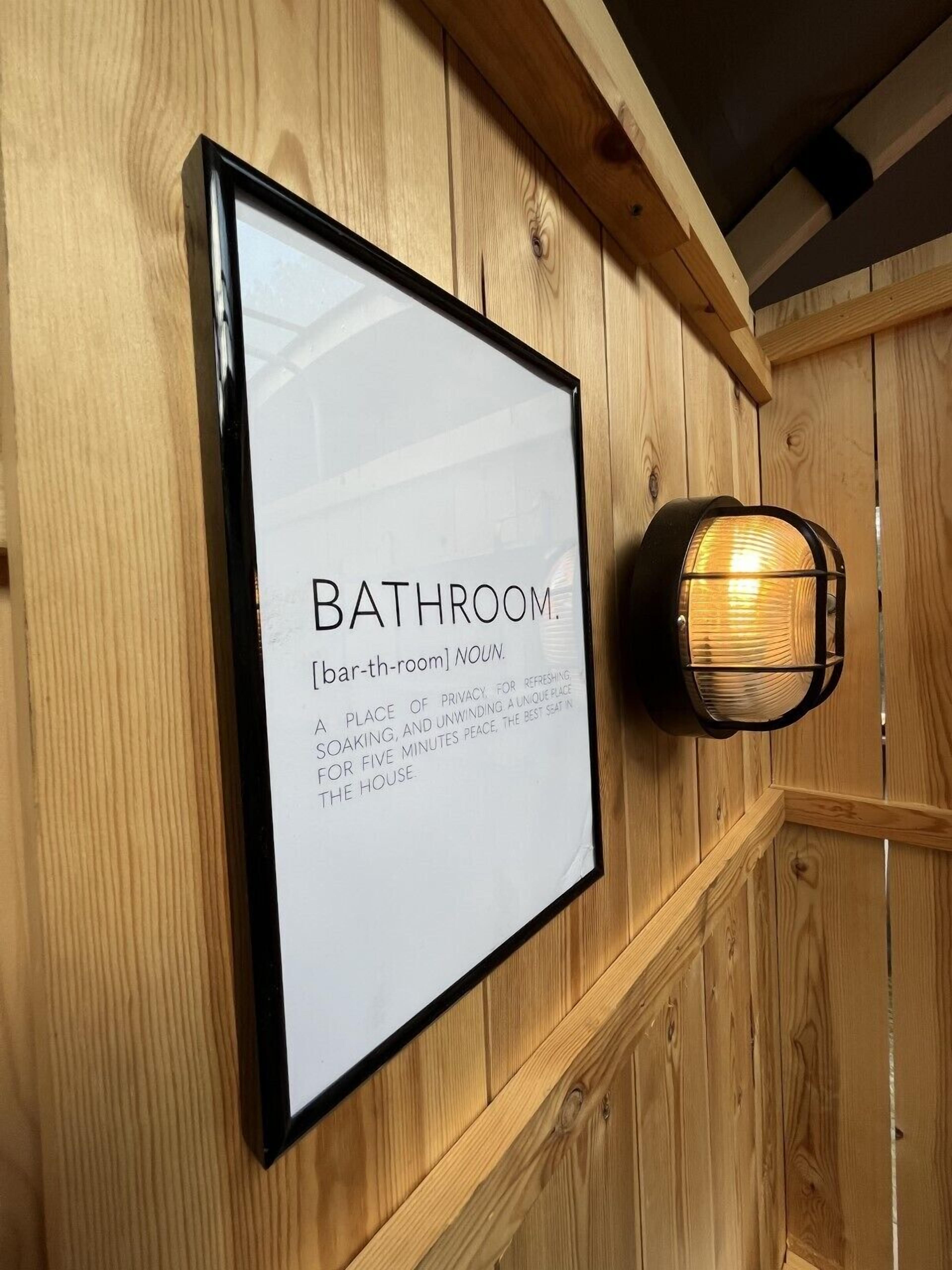 A framed sign on a wooden wall with the word "BATHROOM" and a definition.