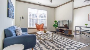 A living room with a blue sofa, a coffee table, a TV, and a patterned rug. - Boulevard Stays Expansive 1BR Suite, Parking (Middletown)