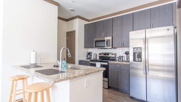 A modern kitchen with granite countertops, stainless steel appliances, and wooden stools. - Boulevard Stays Expansive 1BR Suite, Parking (Middletown)
