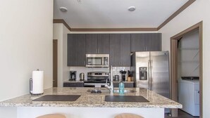 A modern kitchen with granite countertops, stainless steel appliances, and wooden stools. - Boulevard Stays Expansive 1BR Suite, Parking (Middletown)