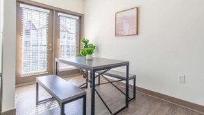 A room with a dark wooden floor, a grey metal table with a bench, a potted plant, and a framed picture on the wall. - Boulevard Stays Expansive 1BR Suite, Parking (Middletown)