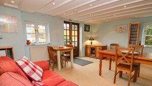 A cozy living room with a red sofa, wooden dining table, and chairs. There is a window with a view of greenery outside. - Penybont Apartment (Aberystwyth)